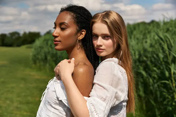 Two young women embrace in a sunlit field, sharing a moment of love and tenderness. — Stock Photo