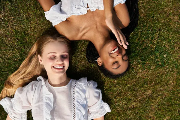 Two young women share laughter and happiness while lying on the grass during a sunny afternoon. — Stock Photo