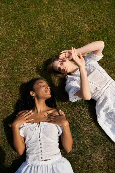 Two beautiful women enjoy each others company while lying on green grass, basking in sunlight — Stock Photo