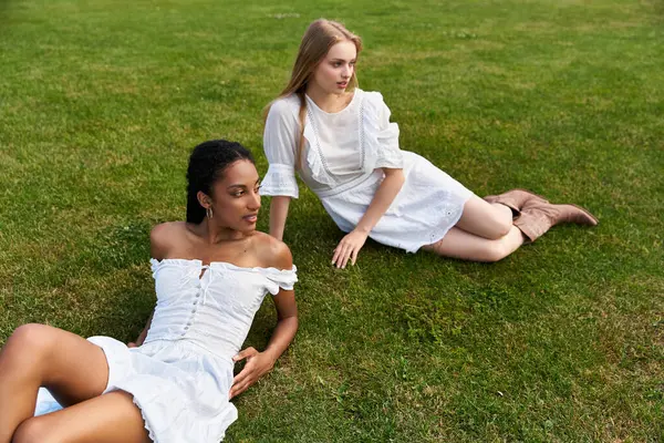 Two young women relax on green grass, sharing smiles and warmth in a joyful moment of romance. — Stock Photo