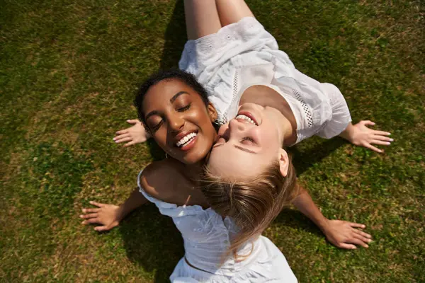 Two beautiful young women embrace each other joyfully while lying on soft grass, radiating love. — Stock Photo