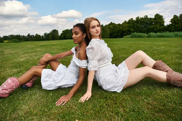 Two women express their love and connection while sitting on soft grass under a clear sky. — Stock Photo