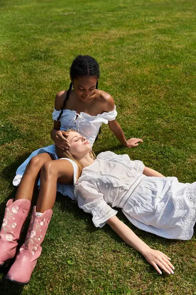 Two joyful women relax under the sun in a lush green park, embodying love and connection. — Stock Photo