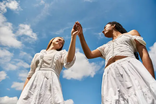 Two young women hold hands in a romantic moment, surrounded by clouds and sunshine. — Stock Photo