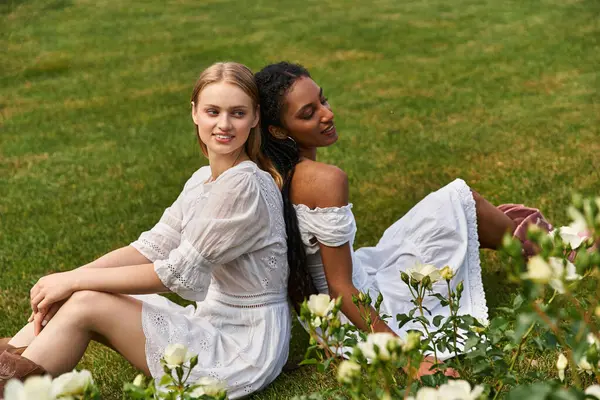 Two women sit happily in a vibrant meadow of blooming roses. — Stock Photo