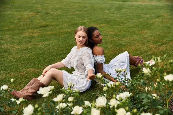In a serene garden, two women sit back to back, joyful among white roses. — Stock Photo