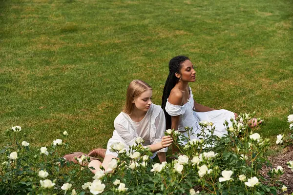 Two women share a tender moment in a lush garden of white roses, reflecting love. — Stock Photo