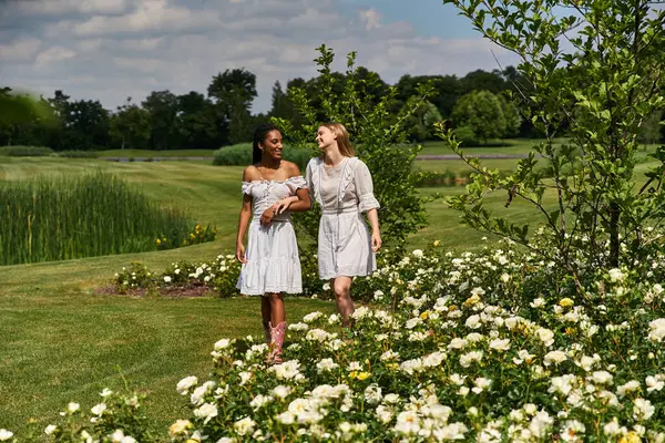 Two young women walk through a vibrant garden, enjoying each others company amid blossoms. — Stock Photo