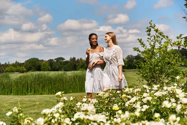 Two young women laugh and share love in a vibrant garden filled with flowers. — Stock Photo