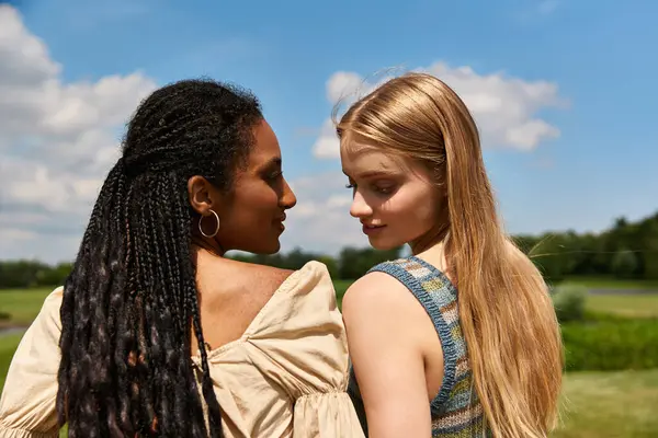 Two young women embrace love and connection in a scenic field under a bright sky. — Stock Photo