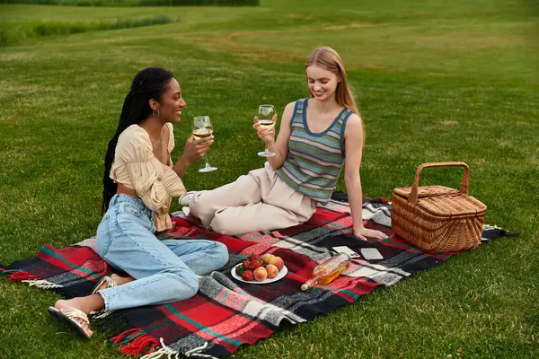 Two young women share a joyful moment, toasting with glasses of wine on a picnic blanket. — Stock Photo