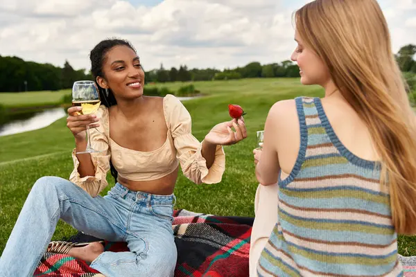 Duas mulheres gostam de rir e morangos em um cobertor de piquenique em um parque exuberante. — Fotografia de Stock