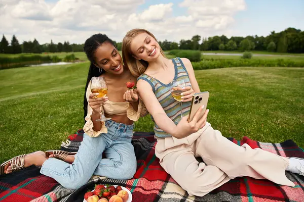 Two joyful women share laughter and a warm moment while taking a selfie during their picnic. — Stock Photo