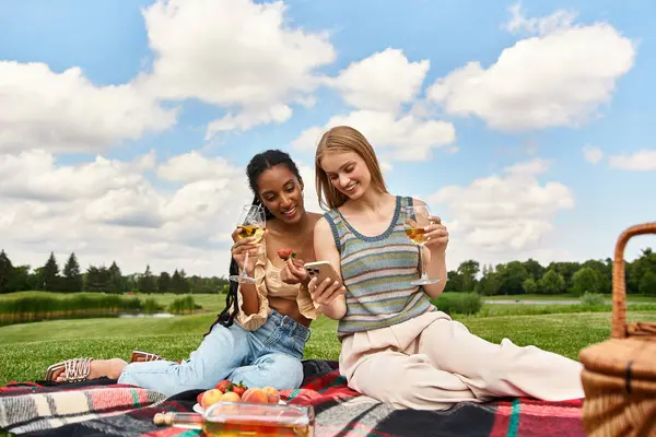 Two joyful women share a moment on a picnic blanket, enjoying drinks and laughter under the clouds. — Stock Photo