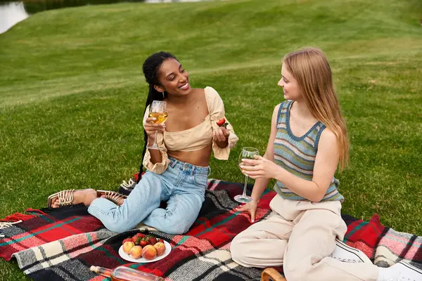 Two young women enjoy a joyful picnic on a sunny day, sharing food and laughter on a blanket. — Stock Photo