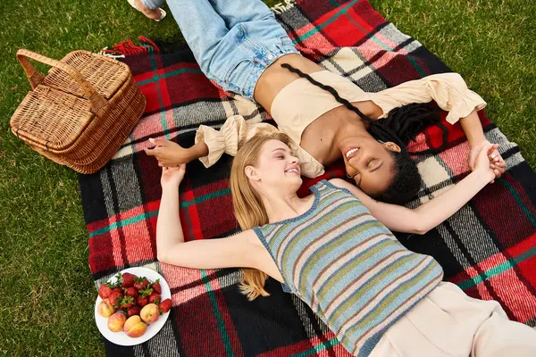 Two beautiful women share a tender moment while lounging on a picnic blanket in the park. — Stock Photo