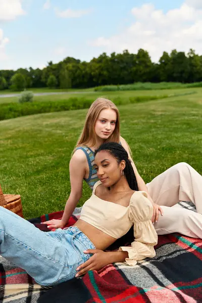 Two young women relax together on a blanket in a vibrant green park, sharing moments of joy. — Stock Photo