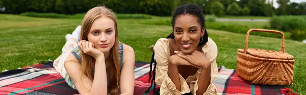 Due giovani donne rilassate su una coperta, ridendo e condividendo momenti gioiosi durante un picnic soleggiato. — Foto stock
