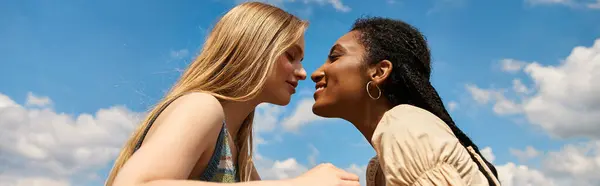 Two beautiful women lean in close, smiling softly while enjoying a sunny day outdoors. — Stock Photo