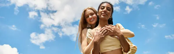 Two beautiful young women embrace under a vibrant blue sky, celebrating their love and joy. — Stock Photo