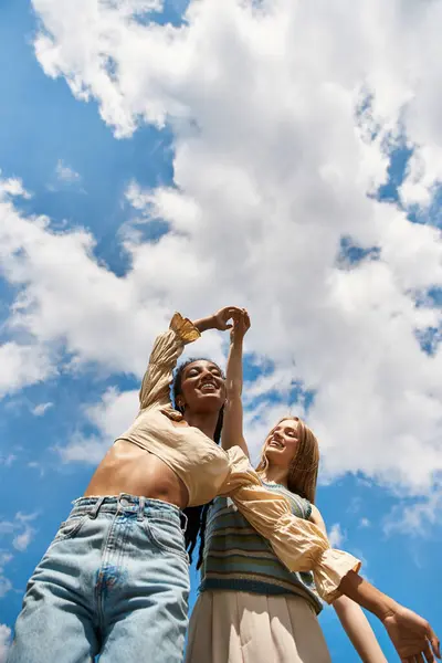 Two young women joyfully dance together, celebrating their love under a vibrant sky. — Stock Photo