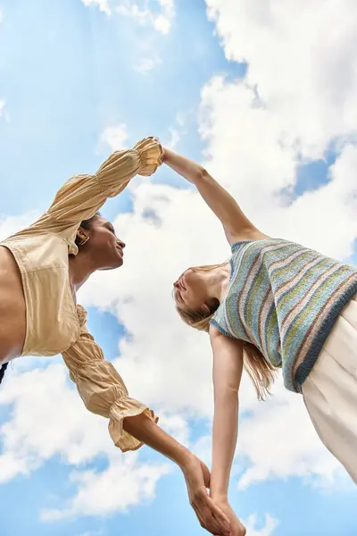 Two women hold hands, joyfully gazing at each other under a beautiful, cloudy sky. — Stock Photo