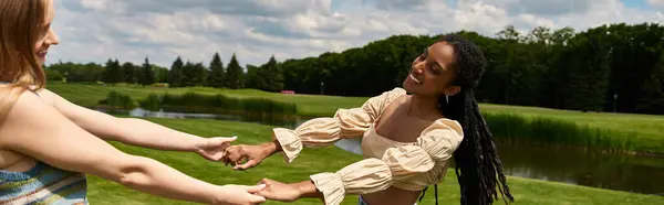 Two beautiful young women hold hands, celebrating love in a vibrant park under a bright sky. — Stock Photo