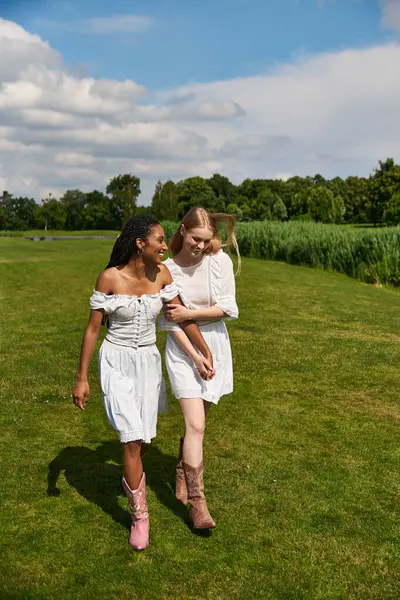Two young women walk hand in hand in a lush park, radiating love and happiness. — Stock Photo