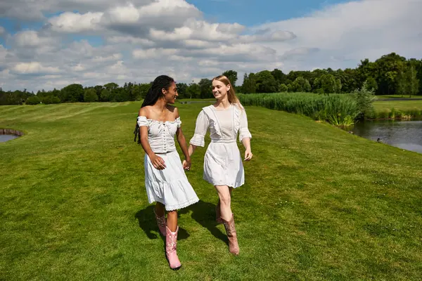 Two beautiful young women stroll together on a lush green landscape, celebrating their love. — Stock Photo