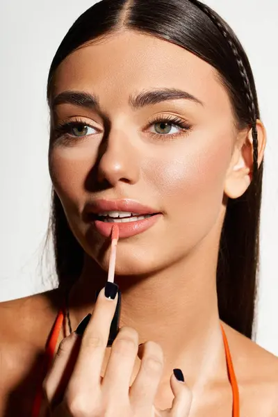 Pretty young woman enhances her look with lip gloss, showcasing summer vibes and sun-kissed skin. — Stock Photo