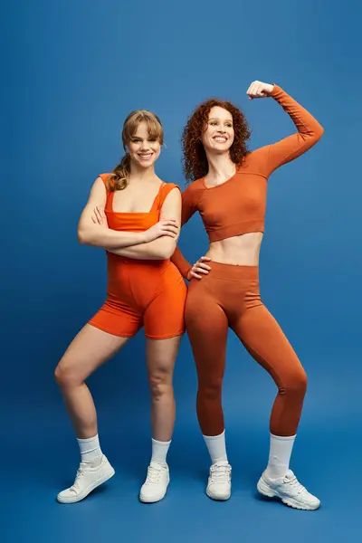 Two young women confidently pose together in vibrant sportswear under studio lights. — Stock Photo