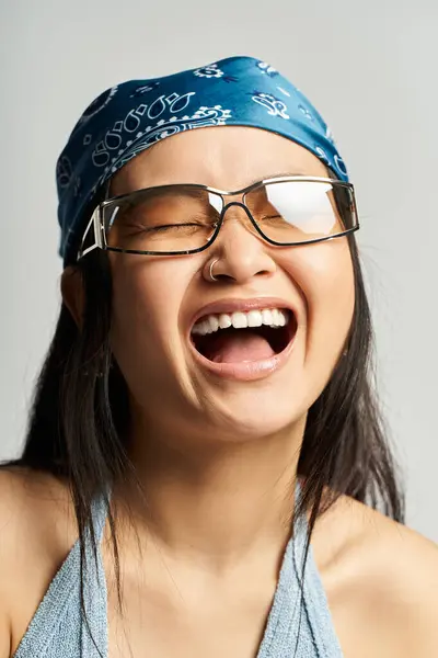 A young Asian woman with glasses and a blue bandana shares a joyful, light hearted moment. — Stock Photo