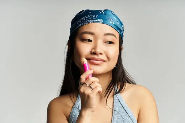Young woman enjoys applying colorful lip balm while showcasing a stylish look and warm smile. — Stock Photo