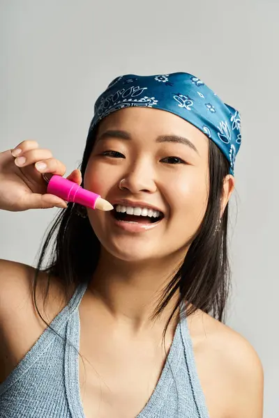 A young Asian woman joyfully holds bright makeup, smiling in a lively atmosphere. — Stock Photo