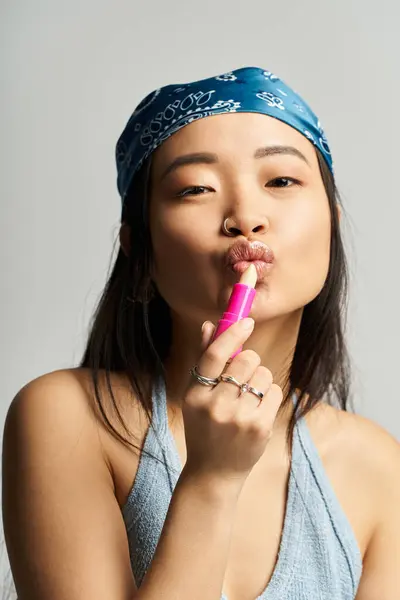 In a modern studio, a young woman playfully applies bright lipstick, exuding confidence. — Stock Photo