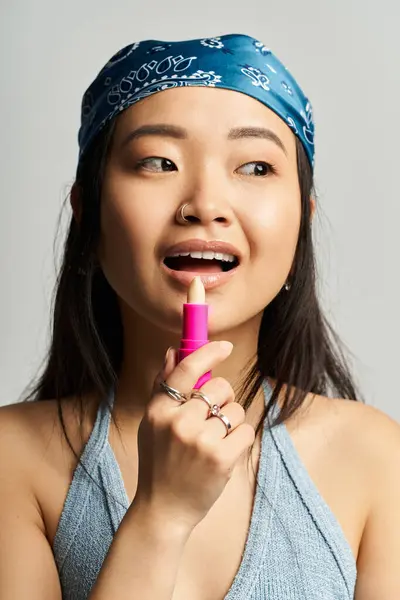 Charming young Asian woman enjoys lip care while showcasing her trendy style in soft lighting — Stock Photo