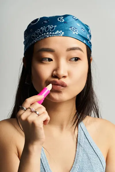 A young Asian woman elegantly applies lip balm, highlighting her unique style and expression. — Stock Photo
