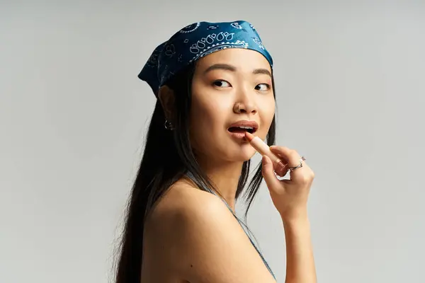 A young beautiful asian woman playfully touches her lip with a finger, showcasing her charm. — Stock Photo