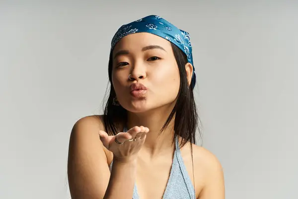 Una bella giovane donna che indossa una bandana soffia giocosamente baci sorridendo, trasudando fascino. — Foto stock