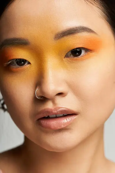 In a close up, a young beautiful Asian woman displays a stunning makeup look with vibrant colors. — Stock Photo