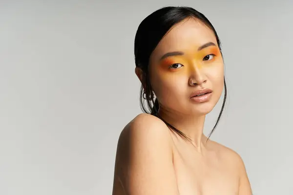 Une jeune femme asiatique met en valeur un maquillage orange vibrant, rayonnant de confiance. — Photo de stock