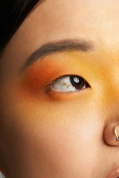 A young Asian woman showcases artistic makeup with vibrant orange and yellow hues. — Stock Photo