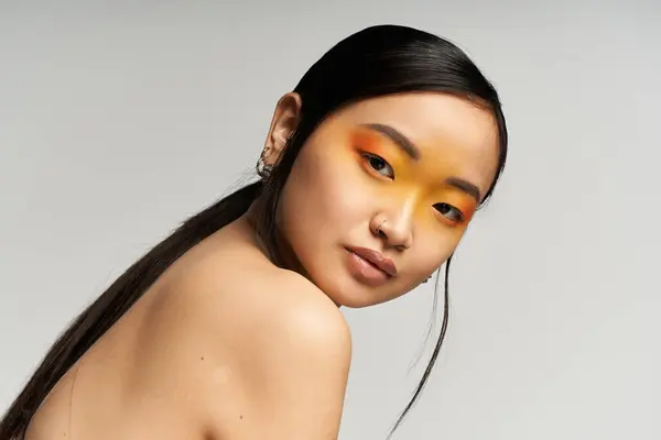 A young Asian woman flaunts vibrant orange and yellow eyeshadow, radiating confidence. — Stock Photo