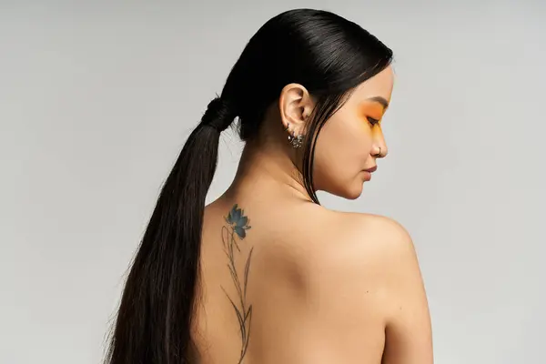 Une jeune femme asiatique se tourne gracieusement, mettant en valeur son tatouage floral avec confiance. — Photo de stock