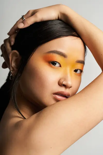 Una joven asiática posa elegantemente con maquillaje naranja en negrita destacando sus rasgos y gracia. - foto de stock