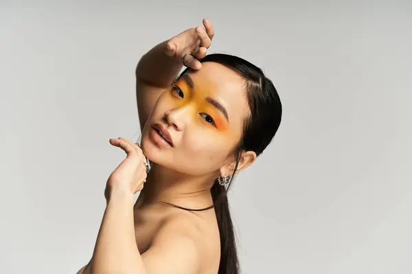 A young beautiful Asian woman poses gracefully with bold orange eye makeup, showcasing artistry. — Stock Photo