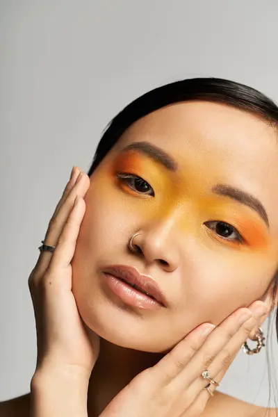 In a calm setting, a young Asian woman flaunts bold orange and yellow makeup, exuding confidence. — Stock Photo