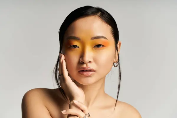 A young beautiful Asian woman poses gracefully, highlighting her artistic makeup with vibrant hues. — Stock Photo
