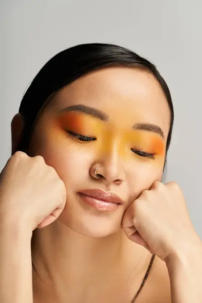 Jeune femme asiatique avec un maquillage jaune et orange vibrant reposant son menton sur ses mains. — Photo de stock