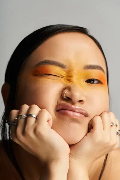 Playful expression emerges from a young Asian woman showcasing vibrant makeup while posing indoors. — Stock Photo